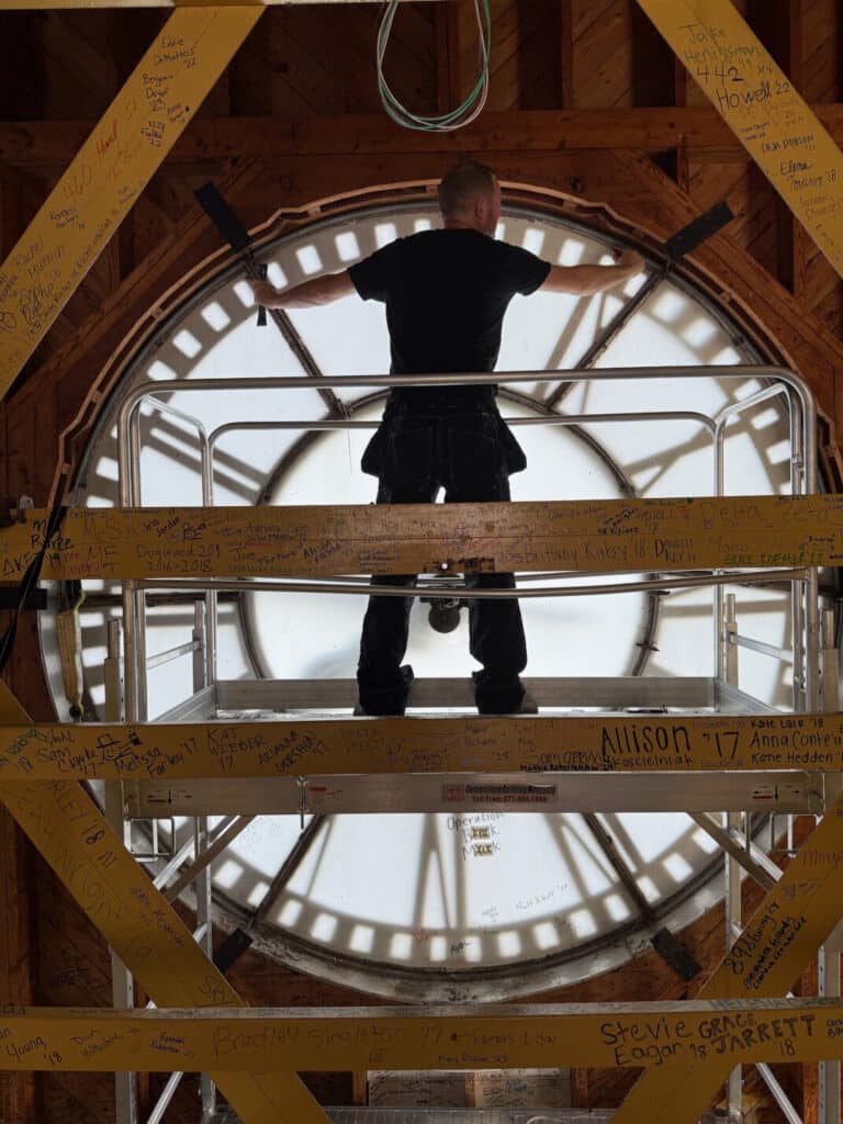 North Carolina, Winston-Salem- Restoration of 4 clocks with man standing on scaffolding repairing large clock