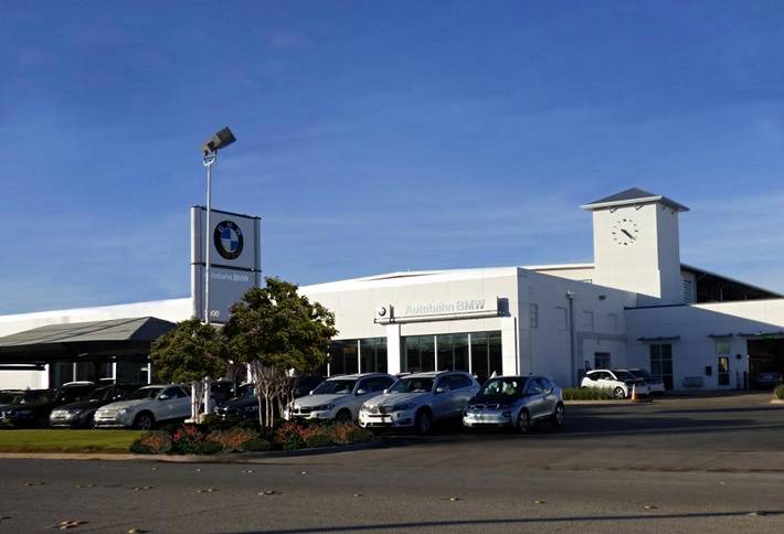 Photo of car dealership, sunny sky, american flag, BMW logo, Lumichron clock tower at Autobahn Motor Group BMW Dealership, Ft. Worth, TX  Skeletal marker silhouette GPS automatic clock by Lumichron