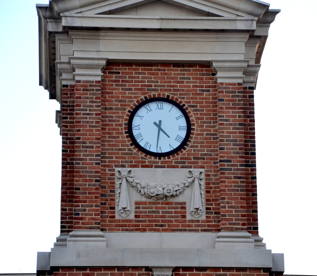 A close up view of a red brick and carved stone clock tower with Roman dial clock