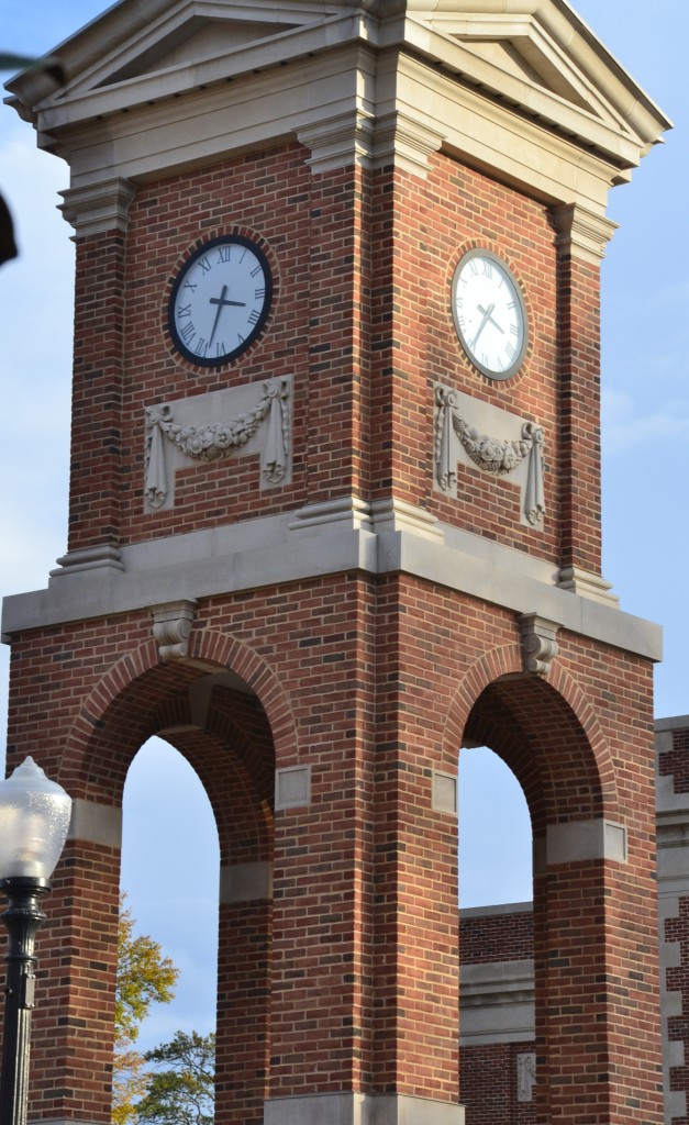 A corner view of red brick and carved stone clock tower with a blue sky background with 2 tower clocks at the University of Alabama