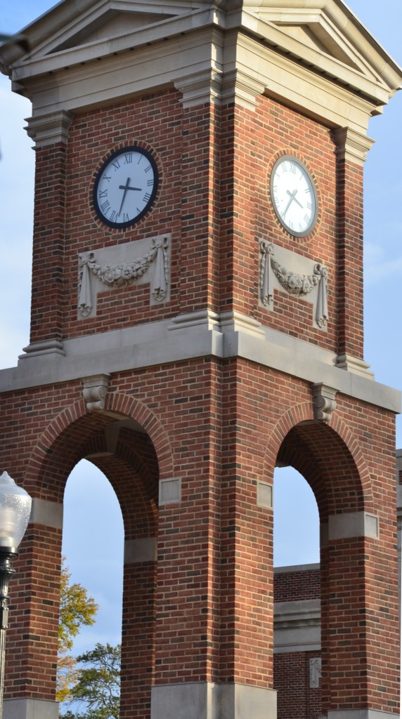 Corner view, close-up of a red brick and carved stone clock tower with a blue sky background with tower clocks at the University of Alabama