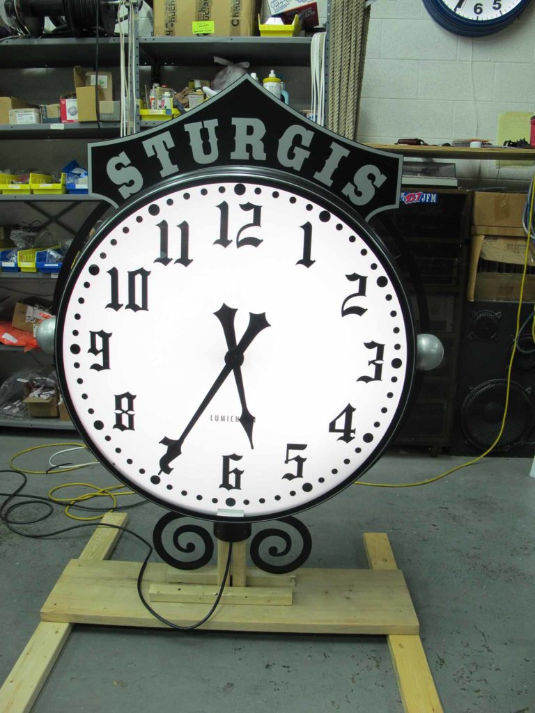 Black and silver Sturgis Post Street clock head on a skid in the workshop 36-inch diameter custom illuminated fully automatic by Lumichron