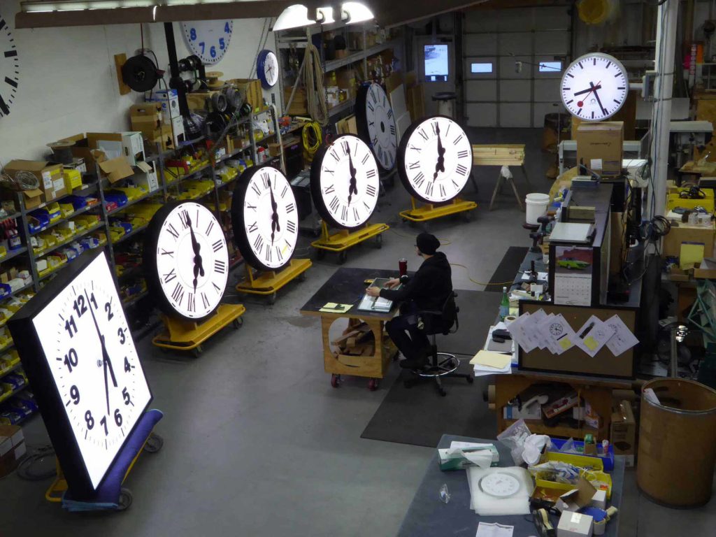 6 illuminated clocks at the Lumichron factory with the talented maestro synchronizing 5 with a masterclock controller