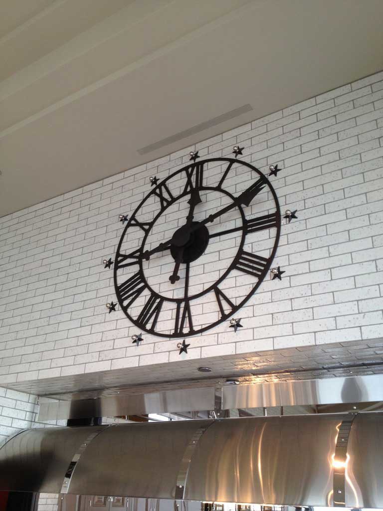 Custom Skeletal Roman dial clock on brick, in a custom kitchen, with decorative chrome and black ball/star indexes by Lumichron