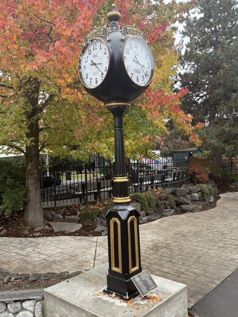 Puyallup WA- 4-way Victorian post clock in a park setting on a pedestal with autumn leaves and trees and rocks