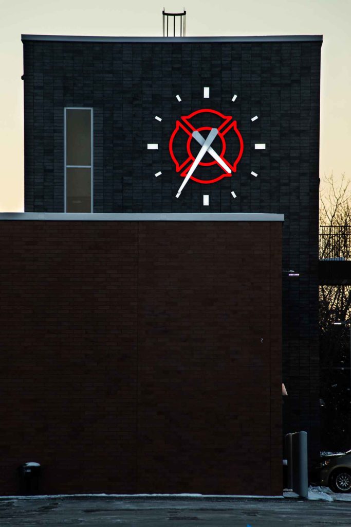 Forest Lake MN Fire Station at dusk, with an illuminated red and white face-lit, 144-inch, skeletal marker silhouette Lumichron Clock