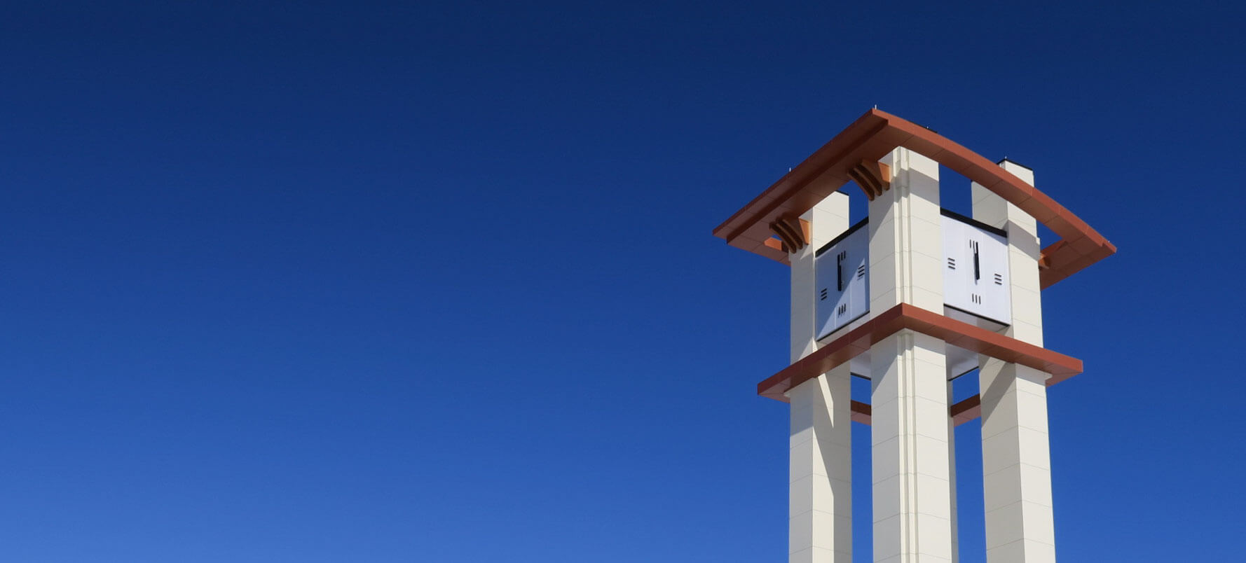 4 sided clock tower at Aurora Highlands new development, blue sky background with 80’ tall open-work white stone with red roofing trim tower with 4 skeletal-type illuminated commercial clocks